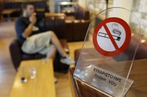 A man smokes a cigarette behind a smoking ban sign in a cafe in Chalandri suburb, north of Athens, August 31, 2010. Greece, will try again to kick the habit by banning tobacco in all public places from September 1. REUTERS/John Kolesidis (GREECE - Tags: POLITICS SOCIETY)